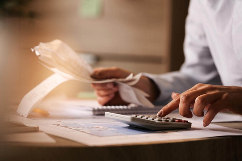 Preparing for Your First Tax Season as a Self-Employed Founder Person in a white shirt uses a calculator while sorting receipts on a desk by candlelight or warm lighting.